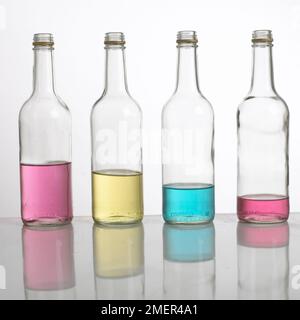 "Tubature per bottiglie" o "xilofono per bottiglie", quattro bottiglie riempite con diverse quantità di acqua colorata, allineate in fila Foto Stock
