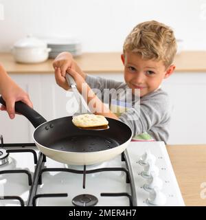 Ragazzo capovolgimento di un pancake in una padella utilizzando una spatola, 4 anni Foto Stock