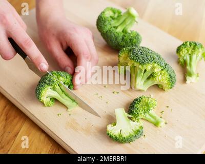 Affettare broccoli crudi su asse di legno Foto Stock