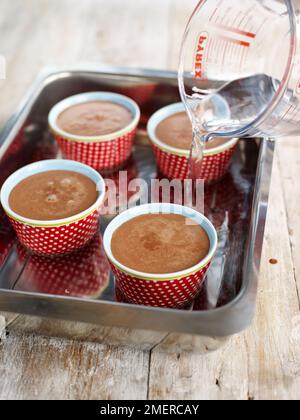 Dessert in pentola di cioccolato in caramelle in teglia da tostatura, acqua calda versata in teglia, pronta per essere cotta in forno Foto Stock