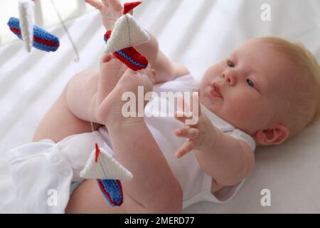 Bambino sdraiato fino a raggiungere la barca a vela a maglia mobile, 5 mesi Foto Stock