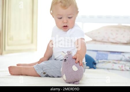 Bambino seduto a giocare con giocattoli di animali morbidi a maglia, 10 mesi Foto Stock