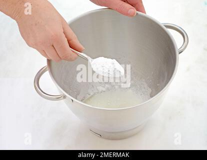 Aggiungere lo zucchero a velo agli albumi per ottenere la glassa reale Foto Stock