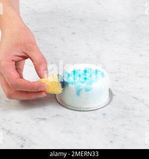 Torta ricoperta di glassa liscia fondente essendo decorata con spugne stampa blu colorante alimentare Foto Stock