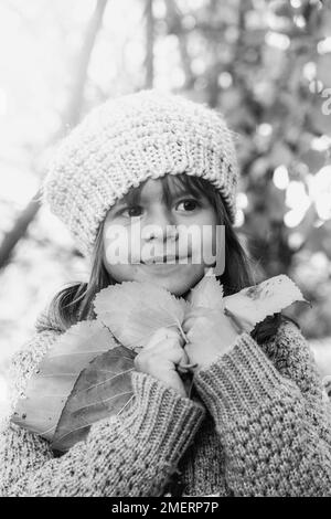 Carina bambina che tiene foglie di acero giallo nelle mani Mentre camminando nel parco soleggiato autunno - Ritratto di bambina in piedi al parco o alla foresta Foto Stock