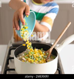 Preparare il risotto di pollo, versare piselli e mais in una pentola di riso e pollo Foto Stock