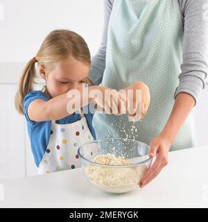 Ragazza strofinando la farina e il burro insieme per far sì che la pasta biscotto, 5 anni Foto Stock