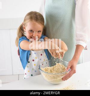 Ragazza strofinando la farina e il burro insieme per far sì che la pasta biscotto, 5 anni Foto Stock