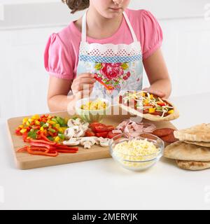 Fare pizze di pitta, Girl Topping pitta pane con selezione di verdure, 8 anni Foto Stock