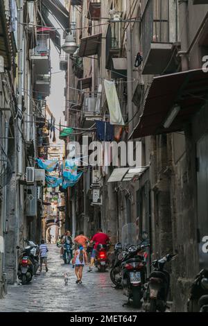 Gente che cammina lungo i vicoli stretti fiancheggiati da edifici in estate, Napoli, Italia. Foto Stock