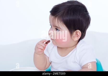 Bambina (40 settimane) che tiene in mano un pezzetto di cibo Foto Stock