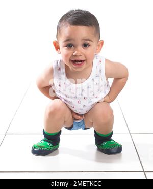 Ragazzo che indossa giubbotto, pantaloni e ciabatte, accovacciato, 15 mesi Foto Stock