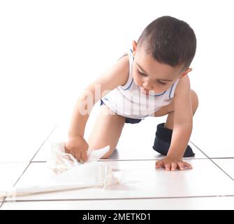 Ragazzo che indossa giubbotto e ciabatte strofinando il pavimento con carta da cucina, 15 mesi Foto Stock