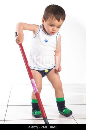 Ragazzo con giubbotto e ciabatte che gioca con un mop, 15 mesi Foto Stock