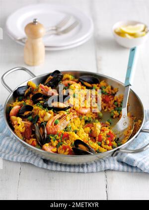 La paella contenente i gamberetti, cozze, piselli e il riso in padella con cucchiaio Foto Stock