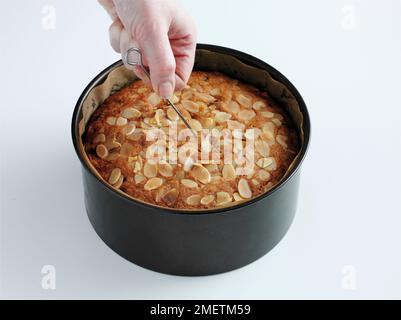 Torta di frutta ricoperta con fiocchi di mandorle, verificando se la torta è cotta, inserendo uno spiedino al centro della torta Foto Stock