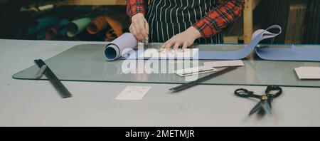 Processo di cucitura. Piccola impresa che fa borse in pelle e tela. La donna taglia la pelle con un coltello speciale sul posto di lavoro. Concetto di personalizzazione Foto Stock