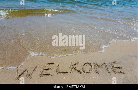 Iscrizione scritta a mano welkome parola sulla spiaggia di sabbia tropicale, viaggio concept card per le vacanze. Foto Stock