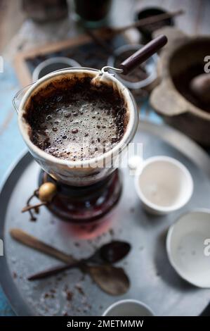 Caffè Touba, caffè che scorre attraverso un panno in una caraffa di vetro Foto Stock