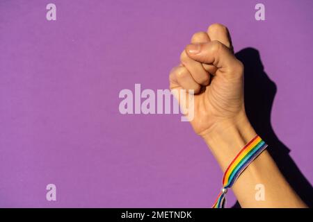 Mano di una donna con pugno chiuso duro sul simbolo di lotta a favore del femminismo, sfondo viola, lotta a favore delle donne, forza femminile, bandiera LGTB Foto Stock