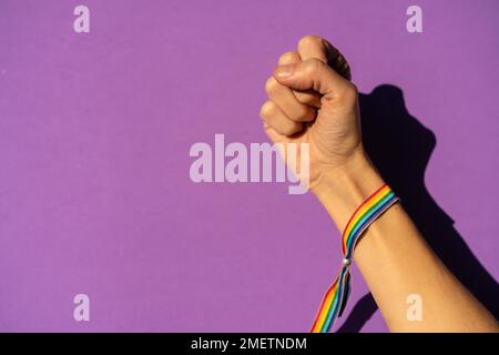 Mano di una donna con pugno chiuso in simbolo femminismo a favore del femminismo, sfondo viola, lotta a favore delle donne, forza femminile, bandiera LGTB Foto Stock