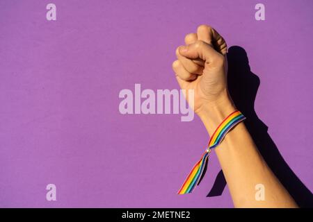 Mano di una donna con pugno chiuso in simbolo femminismo a favore del femminismo, sfondo viola, lotta a favore delle donne, forza femminile, bandiera LGTB Foto Stock