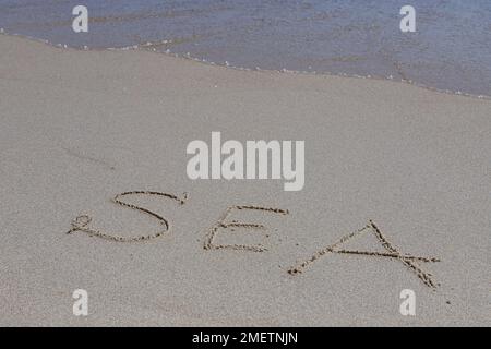 L'iscrizione mare sulla sabbia in riva al mare e l'onda crescente, spiaggia vacanza al mare. Foto Stock