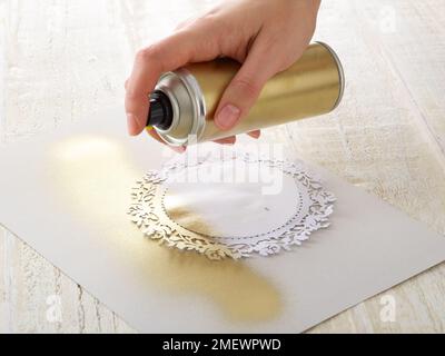 Papiercraft. Fai da te gilding doily fase 2. Con la dima incollata in posizione, spruzzare vernice spray oro Foto Stock