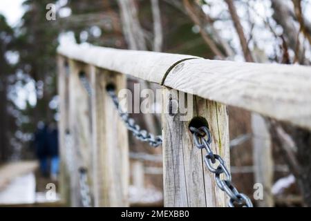 Una ringhiera di legno con una catena metallica al centro e alberi verdi sullo sfondo Foto Stock