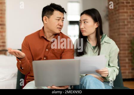 Concetto di crisi finanziaria. Sconvolto la coppia asiatica che controlla i documenti a casa, con problemi di gestione del budget familiare Foto Stock
