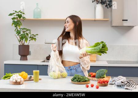 Una bella brunetta estrae le verdure fresche da un sacchetto riutilizzabile. Vegetarismo. Foto Stock