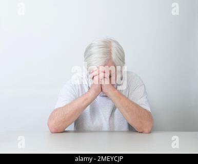 Ripresa orizzontale di un uomo con capelli bianchi seduto da solo nella tristezza, nella preghiera o nella preoccupazione. Sfondo bianco. Molto spazio di copia. Foto Stock