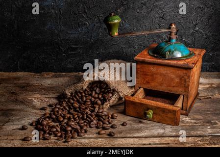 Macinacaffè vecchio con sacchetto di erba e chicchi di caffè sparsi su un tavolo di legno rustico. Foto Stock