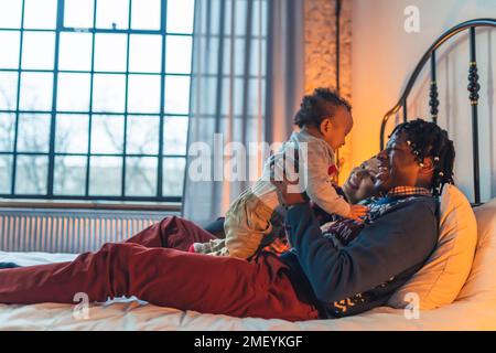 Famiglia multirazziale sorridente di tre persone che si abbraccia e si sdraia su un letto. Foto di alta qualità Foto Stock