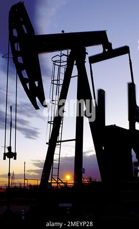 Pump Jack si è posato contro il sole tramontato nel New Mexico. Foto Stock