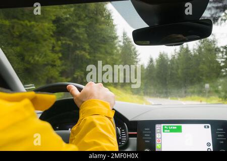 Il turista guida l'auto attraverso il passaggio nelle montagne alpine in giorno piovoso. Il viaggiatore guida l'automobile con la navigazione di Google sulla strada tortuosa fra gli alberi spessi nella foresta di montagna, gennaio 2023, Belluno, Italia Foto Stock