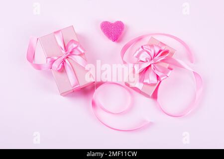 Buon San Valentino, festa della mamma e auguri di compleanno. Cuore rosa  lavorato a maglia e scatole regalo con un arco a nastro satinato su sfondo  rosa Foto stock - Alamy