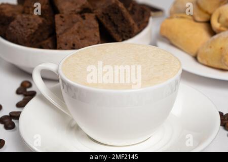 Caffè con crema di latte in una tazza di ceramica bianca e torta al cioccolato sul tavolo. Delizioso cappuccino aromatico, colazione Foto Stock