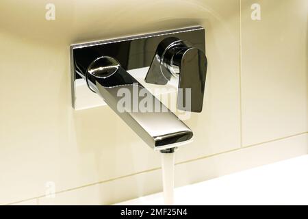 L'acqua si riversa da un rubinetto in acciaio inossidabile cromato lucido dal design moderno sopra il lavandino in marmo nel bagno dell'hotel Foto Stock