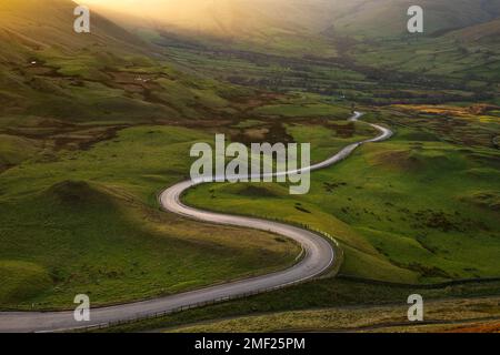 Lunga strada di campagna tortuosa che conduce attraverso la campagna britannica vista dal MAM Tor nel Parco Nazionale del Peak District. Foto Stock
