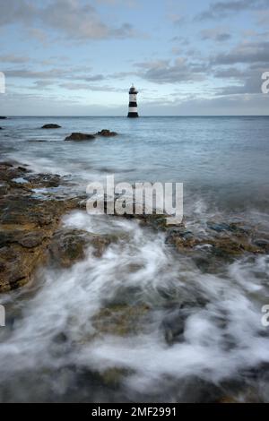 Penmon Point Lighthouse sulla costa di Anglesey, Galles del Nord. Onde che si infrangono in primo piano all'alba. Foto Stock