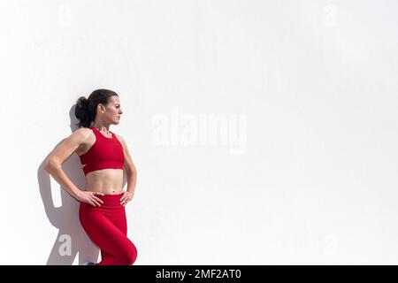 Donna sportiva con le mani sui fianchi appoggiate al sole su una parete bianca. Foto Stock