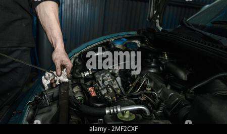 Raccogliere un riparatore non riconoscibile utilizzando l'astina di livello dell'auto per misurare il livello dell'olio motore Foto Stock