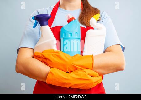 Donna con guanti e grembiule che tiene prodotti detergenti su sfondo blu Foto Stock