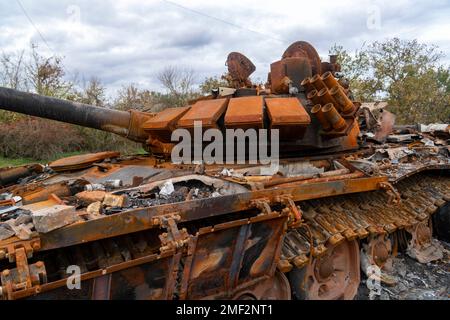 Campagna dopo la battaglia. Un carro armato da battaglia distrutto e bruciato si trova sulla strada (primo piano). Guerra in Ucraina. Invasione russa dell'Ucraina Foto Stock