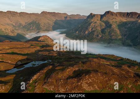 Veduta aerea della nebbia nella valle in una mattinata soleggiata. Langdale Pikes da sopra Lingmoor Fell, Lake District, Regno Unito. Foto Stock