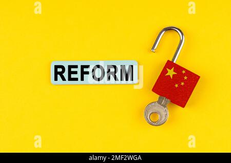 Su una superficie gialla, una serratura aperta con l'immagine della bandiera della Cina e un adesivo con l'iscrizione - RIFORMA Foto Stock