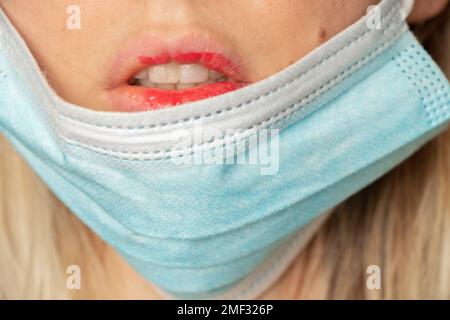 faccia di una ragazza in una maschera medica con rossetto rosso sulle labbra primo piano, medicina, una ragazza in una maschera medica Foto Stock