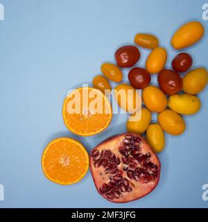 Arance, kumquat, melograno e pomodori ciliegini rossi su sfondo blu pastello. Piatto stratificazione di frutta fresca. Ispirazione estiva Foto Stock