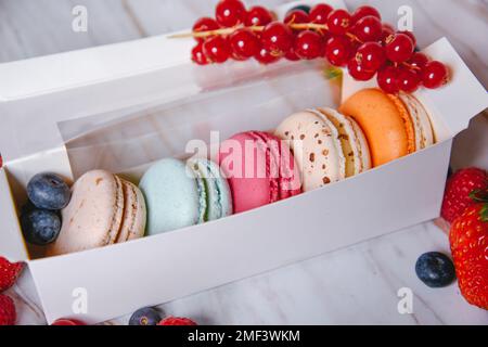 Macaronis in una scatola bianca con una finestra trasparente. Colore dessert, rosa, menta, macaroon blu e arancio. Fragole, lamponi, mirtilli e f Foto Stock